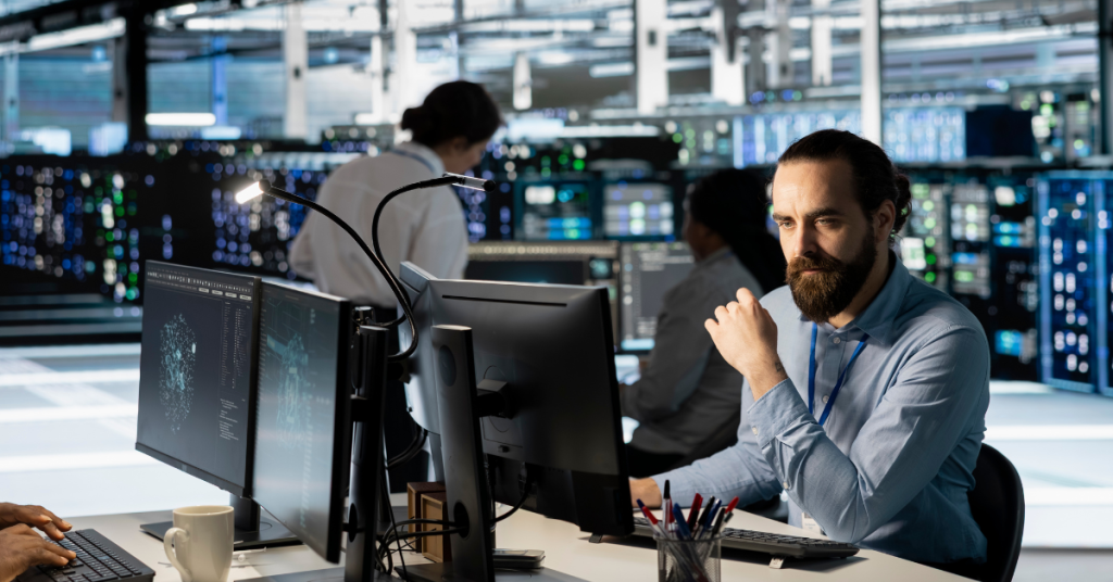 A focused IT specialist monitoring multiple computer screens in a high-tech data center, representing outsourced operational efficiency.