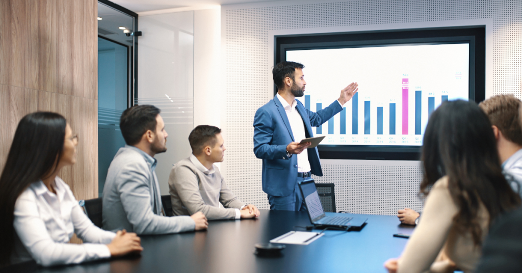 A business professional presenting data to a team during a strategy meeting, showcasing growth charts on a large screen.