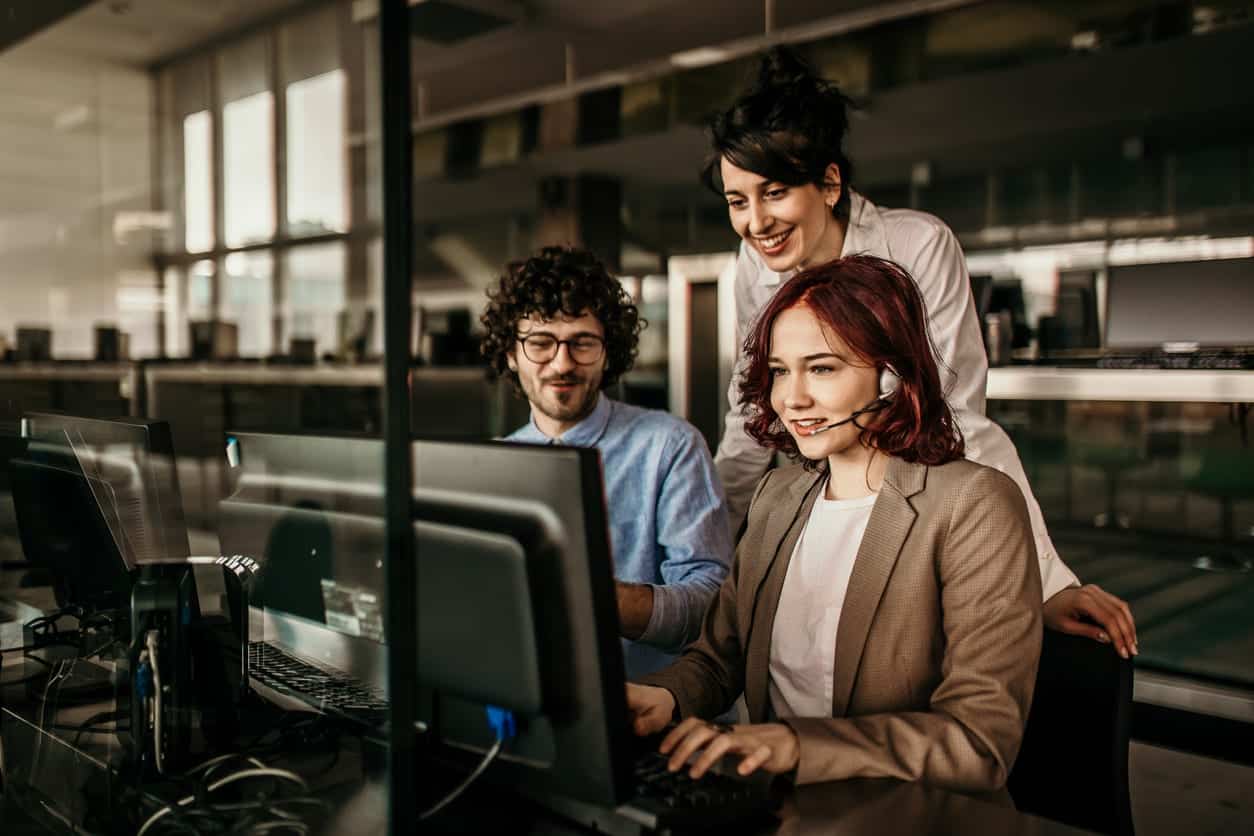 three-IT-professionals-gathered-around-computer-monitor-at-desk-in-office