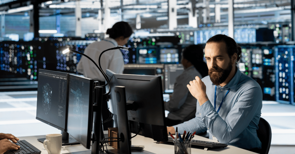 A focused IT specialist monitoring multiple computer screens in a high-tech data center, representing outsourced operational efficiency.