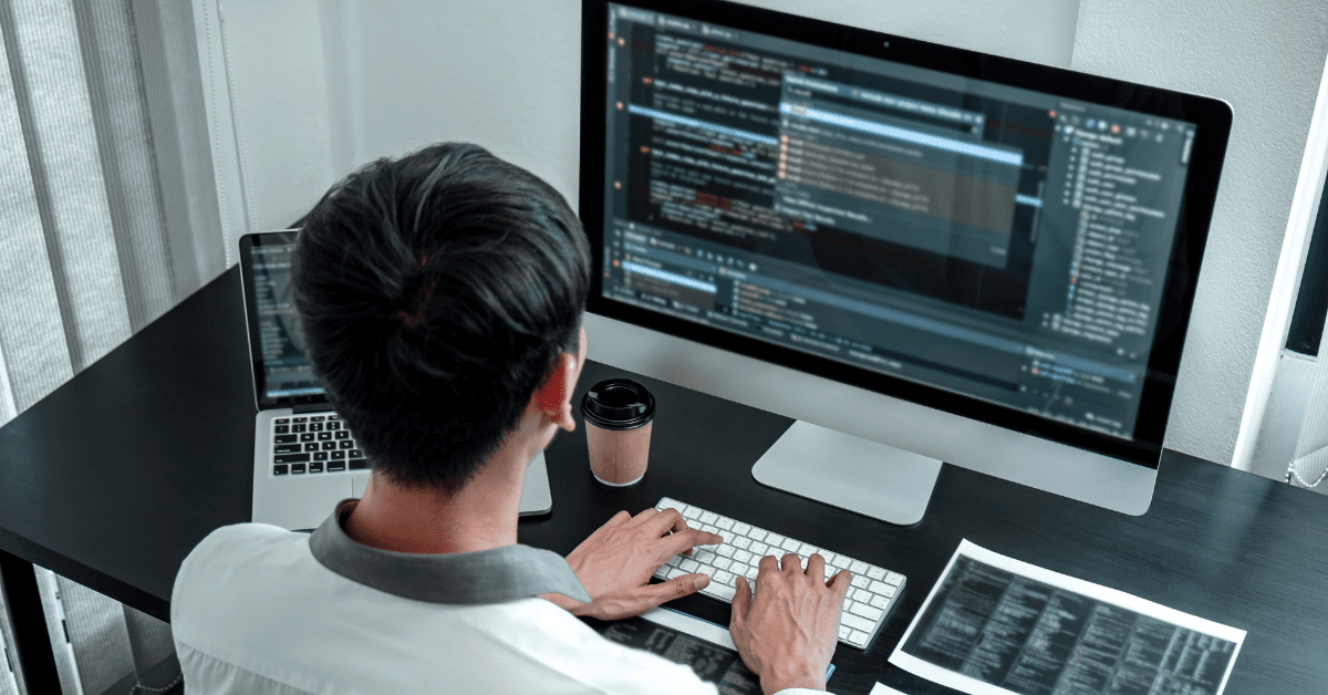 A developer working at a large monitor with code on screen, illustrating streamlined operations through outsourced IT programming.