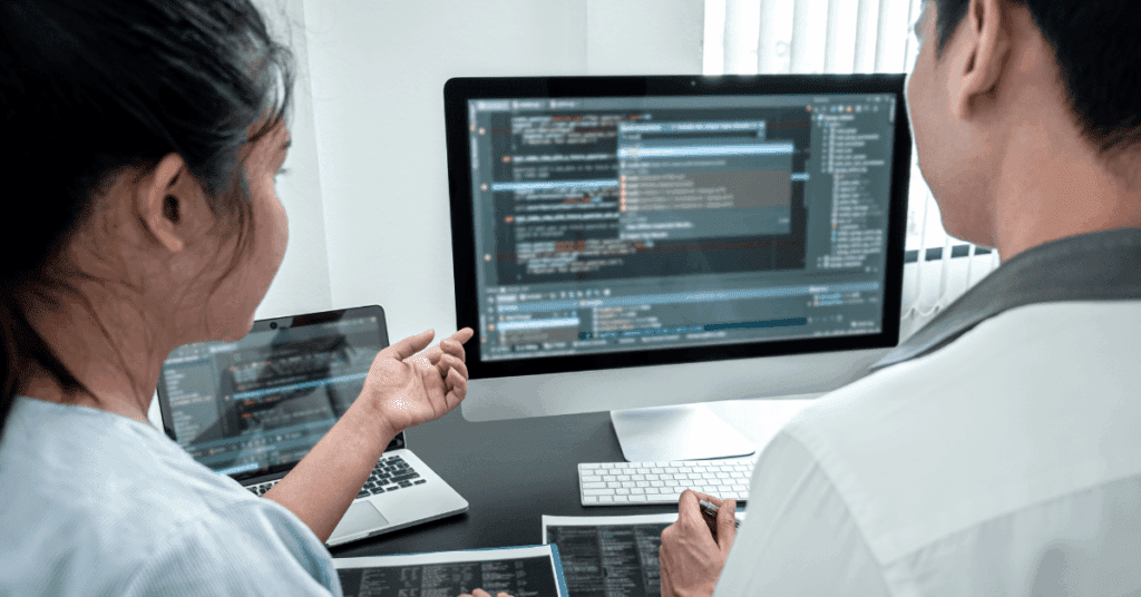 Two developers reviewing code on a large screen together, illustrating teamwork and continuous improvement in the software development life cycle.
