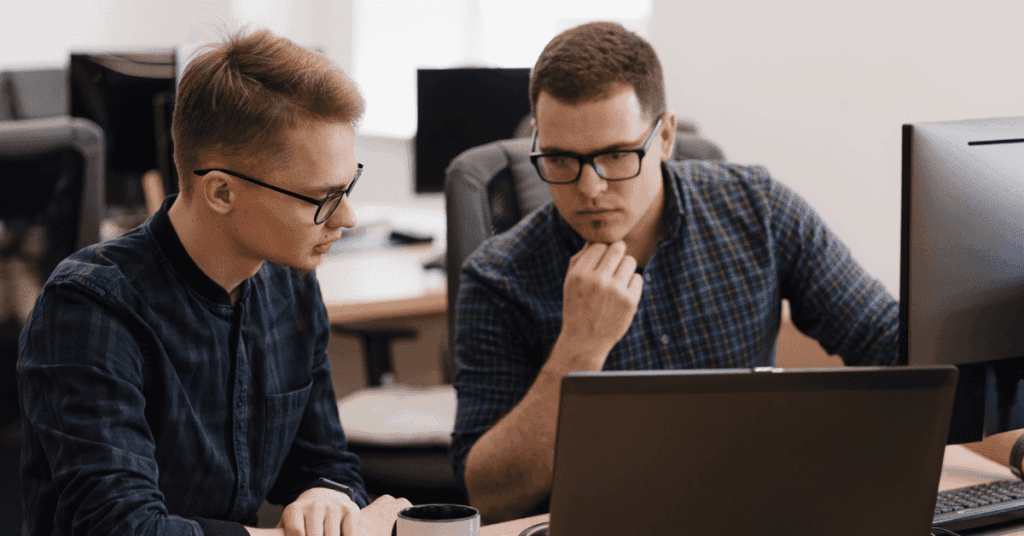 Two IT professionals focused on coding and discussing solutions together in a modern office setting.