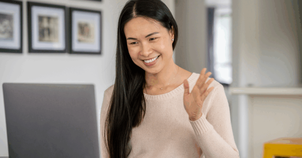 Smiling woman waving during a video interview on her laptop from a home office.
