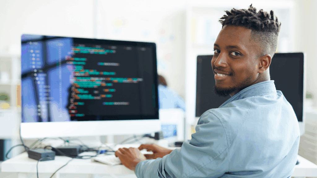Smiling software developer working at a desk with code on a dual-monitor setup, representing nearshore IT talent collaboration.