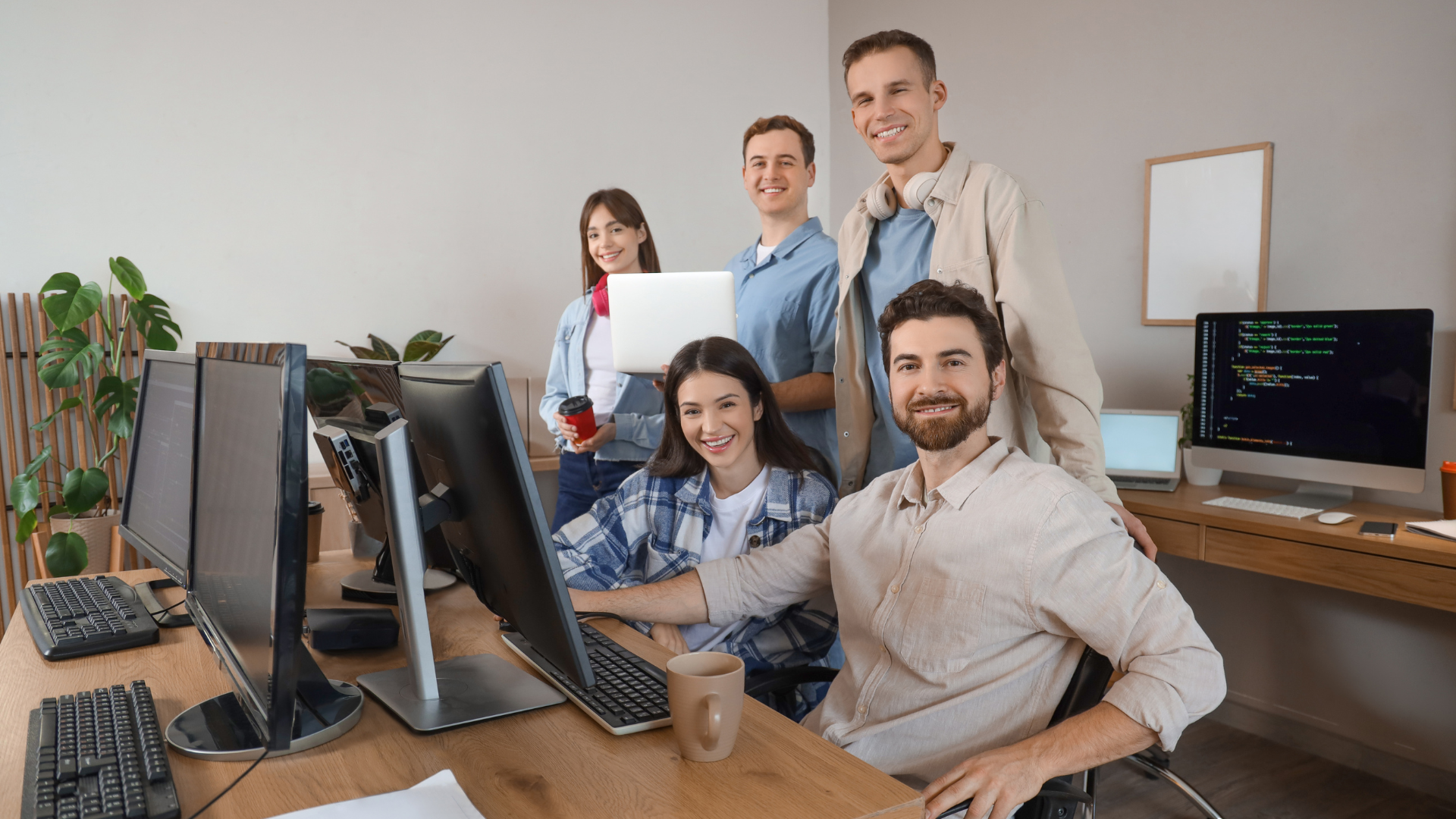 Smiling software development team working together in a modern office with multiple monitors and coding screens.