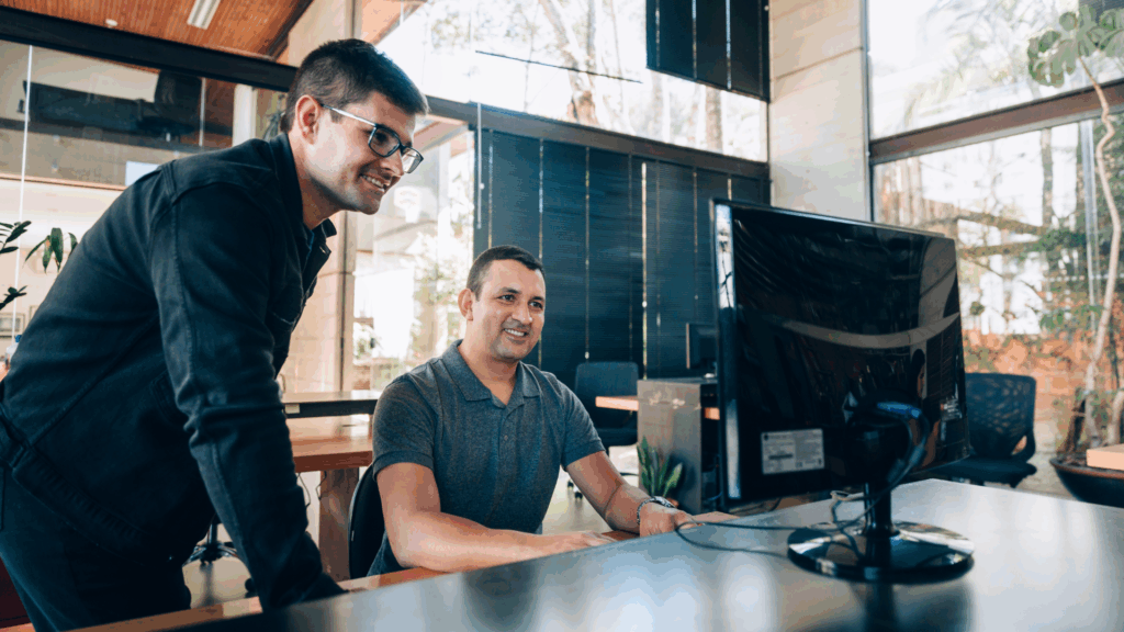 Two smiling developers working together at a computer in a modern, well-lit office, symbolizing teamwork and nearshore development culture.