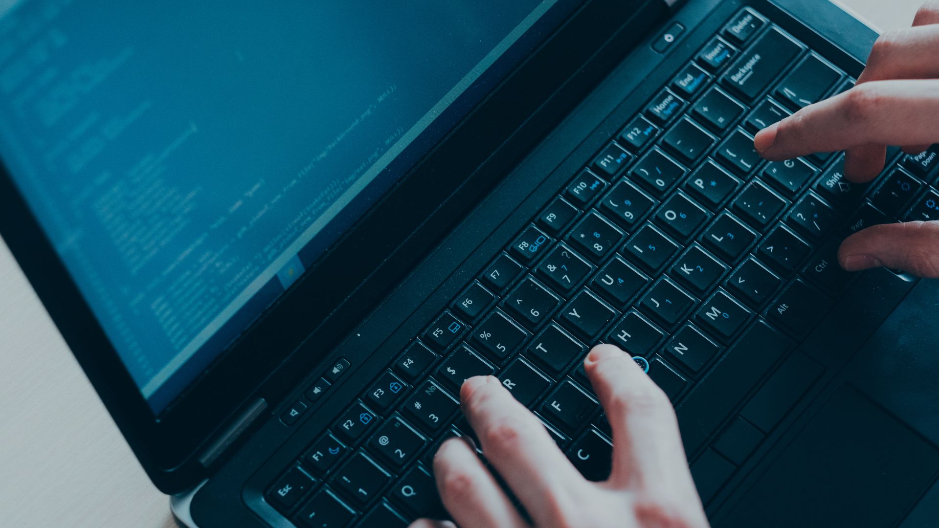 parallelstaff- Hands typing on a laptop keyboard with code displayed on the screen, suggesting software development or programming activity.