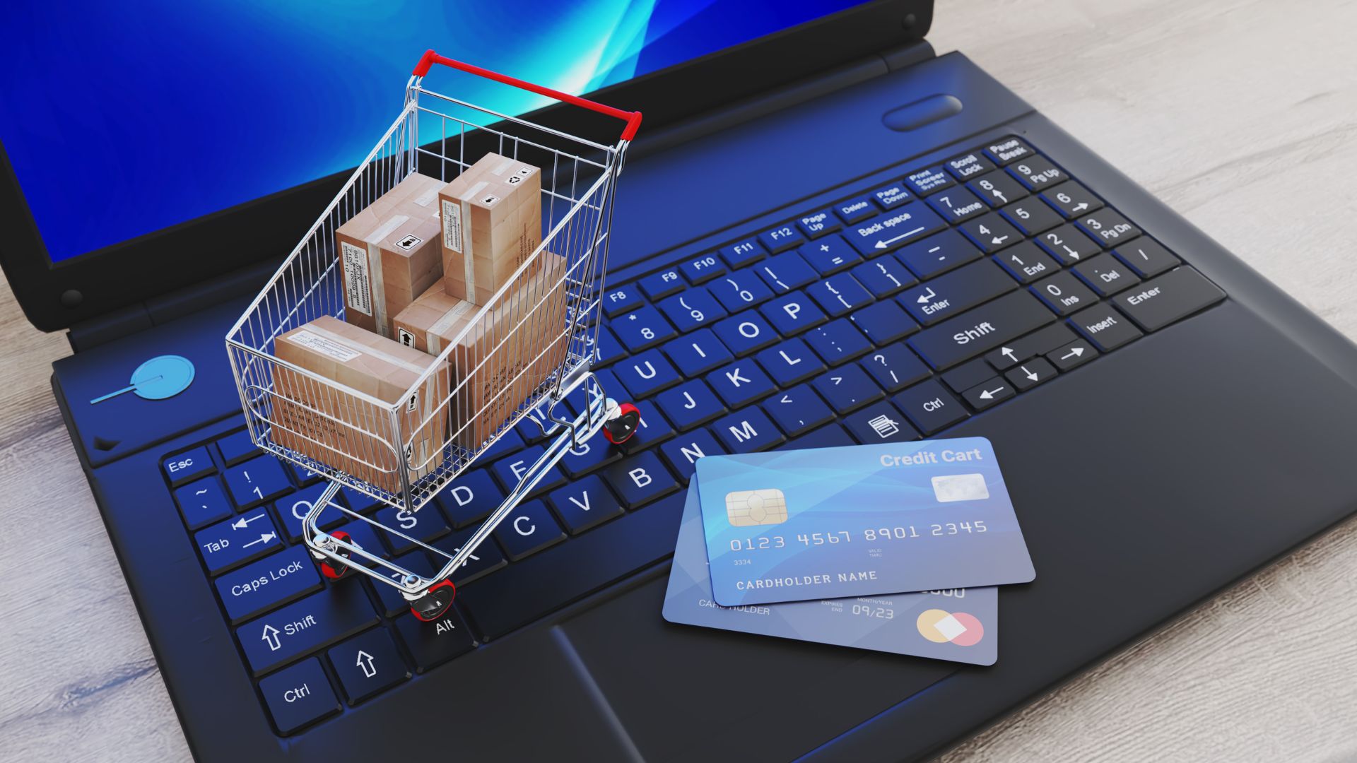 parallelstaff- A miniature shopping cart with cardboard boxes sits on a laptop keyboard next to two credit cards, symbolizing online shopping and e-commerce.