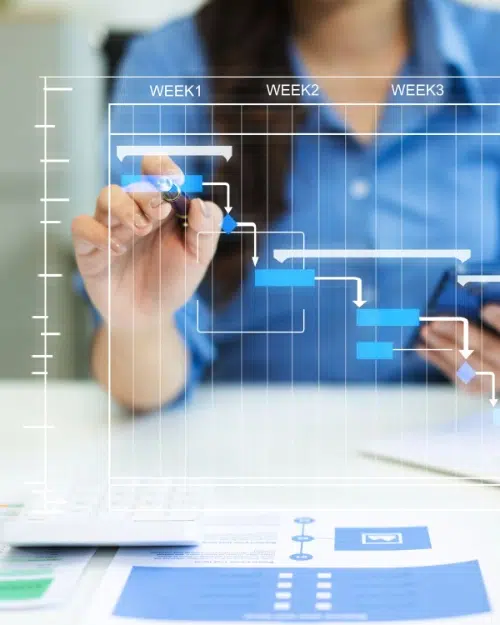 parallelstaff- A person in a blue shirt uses a pen to interact with a digital Gantt chart displaying tasks and timelines for three weeks, with documents and a calculator on the desk.