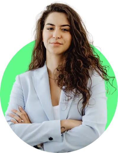 parallelstaff- A woman with long, curly brown hair wearing a light blue blazer stands with arms crossed, smiling slightly. The background is a bright green circle.