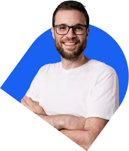 parallelstaff- A smiling man with glasses and a beard, wearing a white t-shirt, stands with his arms crossed in front of a blue geometric background.