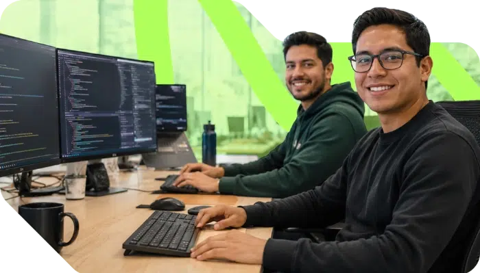 parallelstaff- Two people sit at desks with large monitors displaying code, smiling at the camera in a modern office setting with green accents.